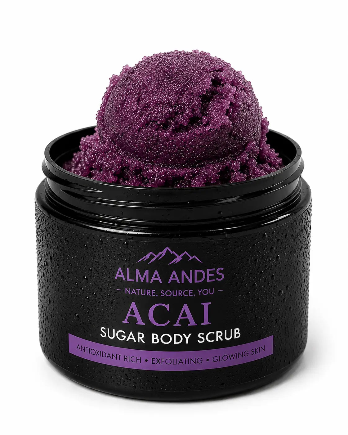 A black jar of Alma Andes Acai Sugar Body Scrub, shown open with a scoop of deep purple scrub visible inside. The jar has a textured black finish with condensation droplets, and the label features purple and white text.