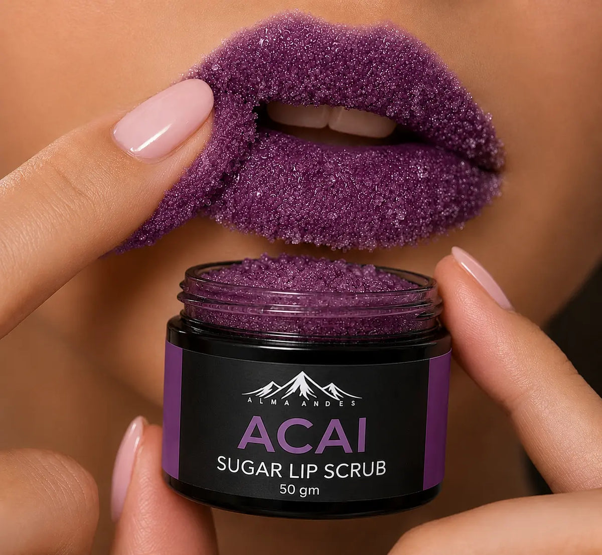 A close-up of a person's lips coated with sparkling purple sugar lip scrub, with fingers lifting one side of the lips to show the scrub texture. A small black jar labeled 'ALMA AND ES ACAI SUGAR LIP SCRUB 50 gm' is held in the foreground.