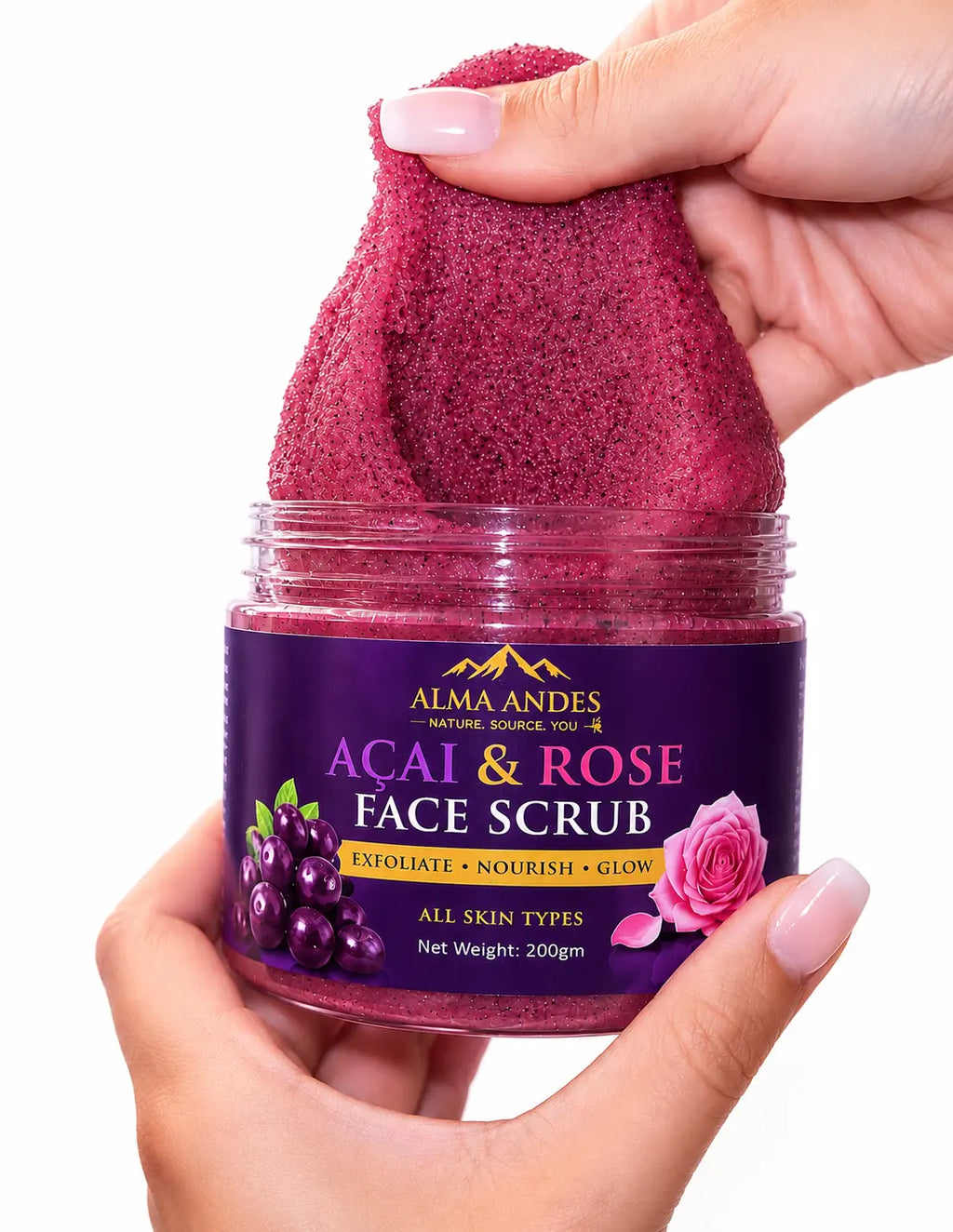 A hand holds an open jar of Almaandes Acai & Rose Face Scrub, showing the deep purple scrub being stretched between the fingers against a clean white background.
