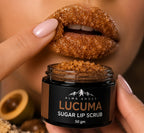A close-up of a person holding an open jar of ALMA ANDES LUCUMA SUGAR LIP SCRUB, with their lips coated in the brown sugar scrub above it. The jar is held by hands with pale pink manicured nails, and a halved lime is visible in the blurred background.