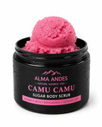 A black jar of Alma Andes Camu Camu Sugar Body Scrub, shown open with a scoop of bright pink scrub on top, against a white background.