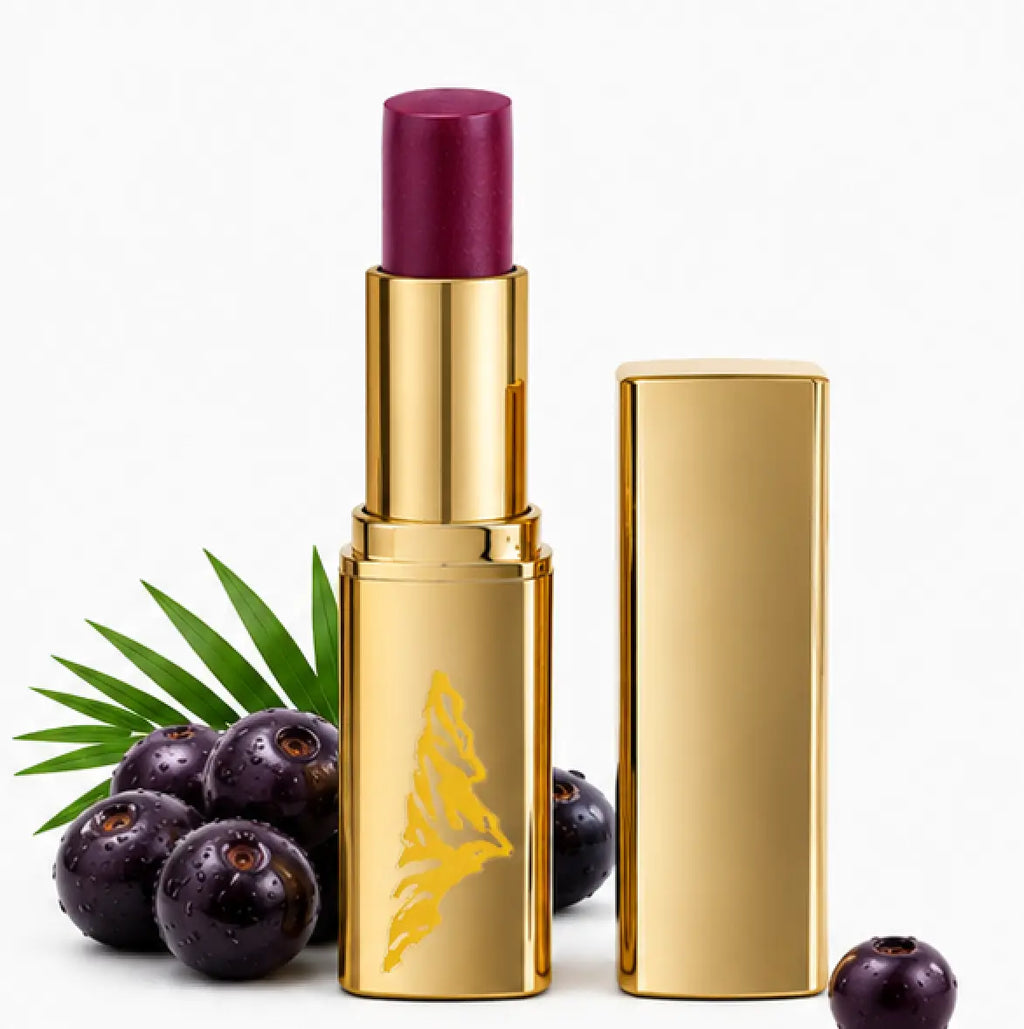Gold lipstick with purple shade and open cap on a white background with dark berries and green leaves.