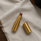 Lipstick with gold case on a textured beige fabric background